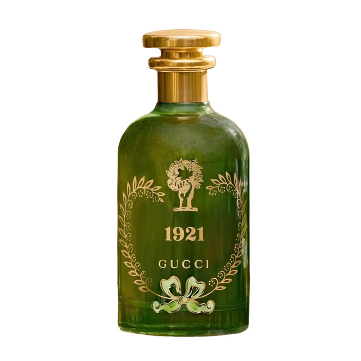 Green Gucci 1921 perfume bottle with gold cap on a decorative surface with plants in the background